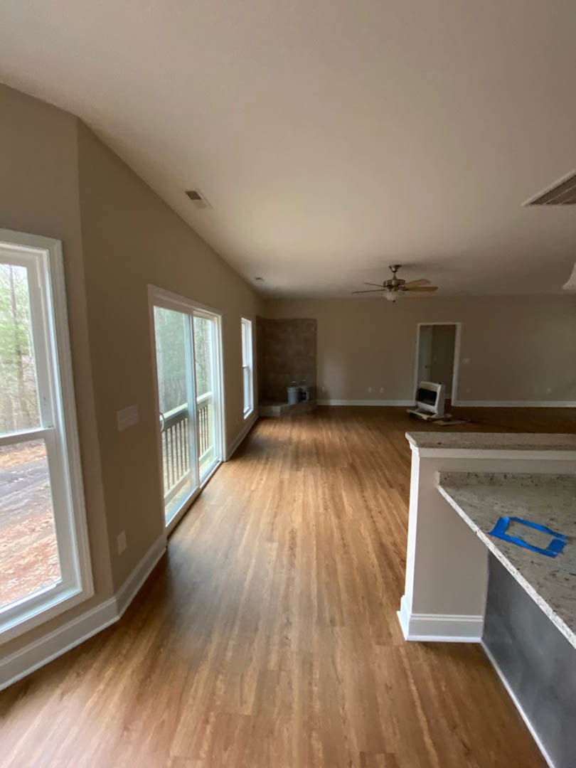 Hardwood floor room with ceiling fan and light, window overlooking outdoors, blue tape marking on floor, partial view of computer screen