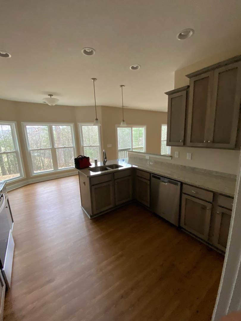 Kitchen with light wood flooring, white cabinetry, stone countertops, large windows overlooking trees, stainless steel appliances