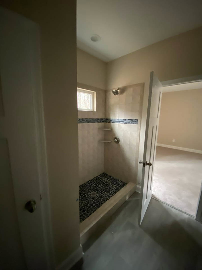 Bathroom with black and white tiled shower, open white door, corner shelf, and window letting in natural light
