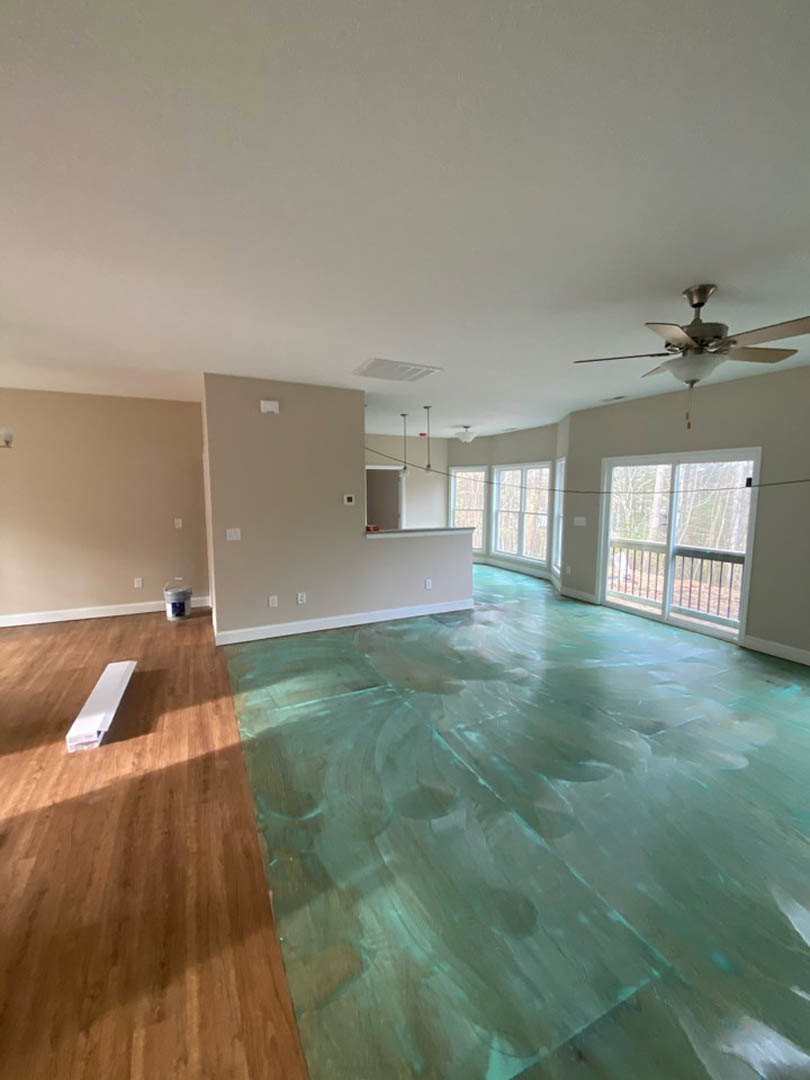 Green laminate flooring, wood ceiling with fan and light, sliding glass door with metal railing, white rectangular object on wooden surface, white strip across wood floor.