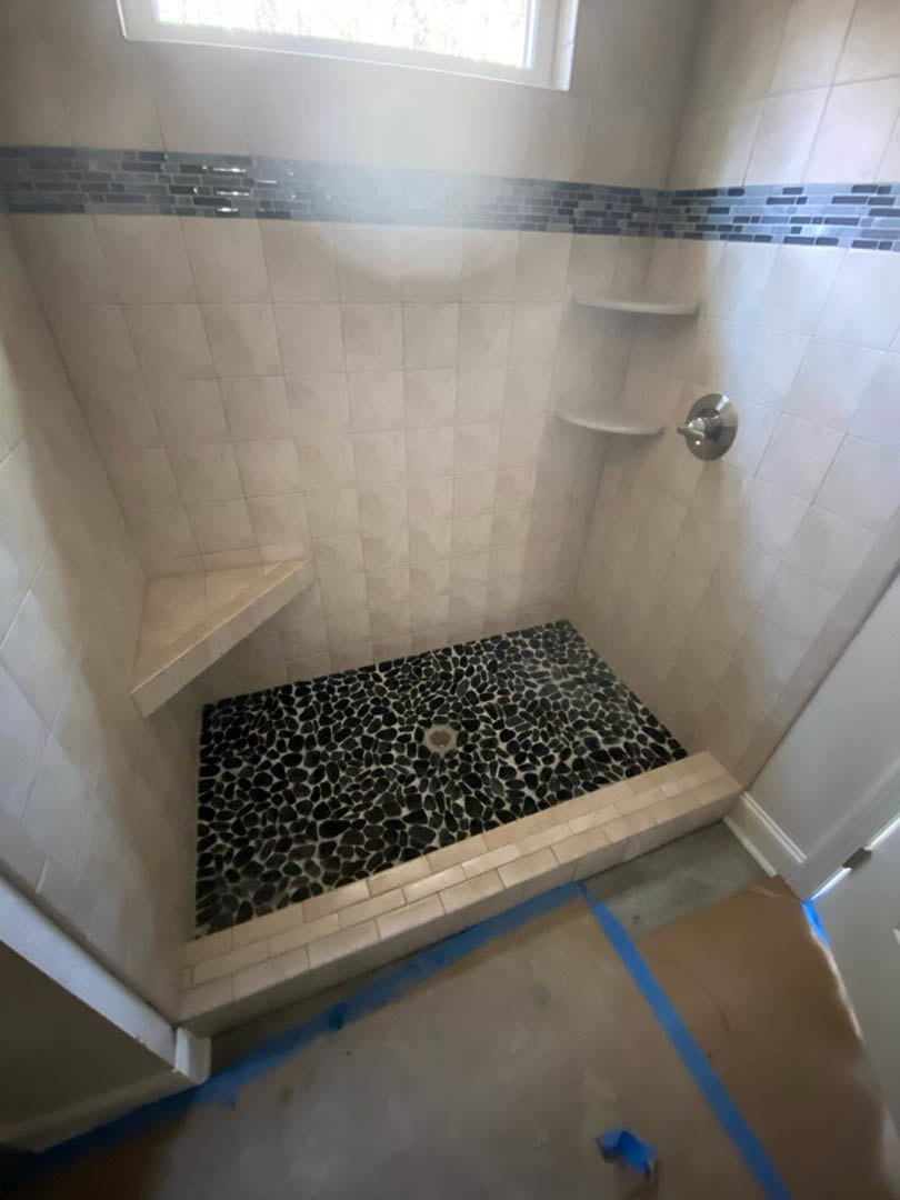 Shower with black and white geometric tile floor, white marble walls, chrome plumbing fixtures, and glass enclosure