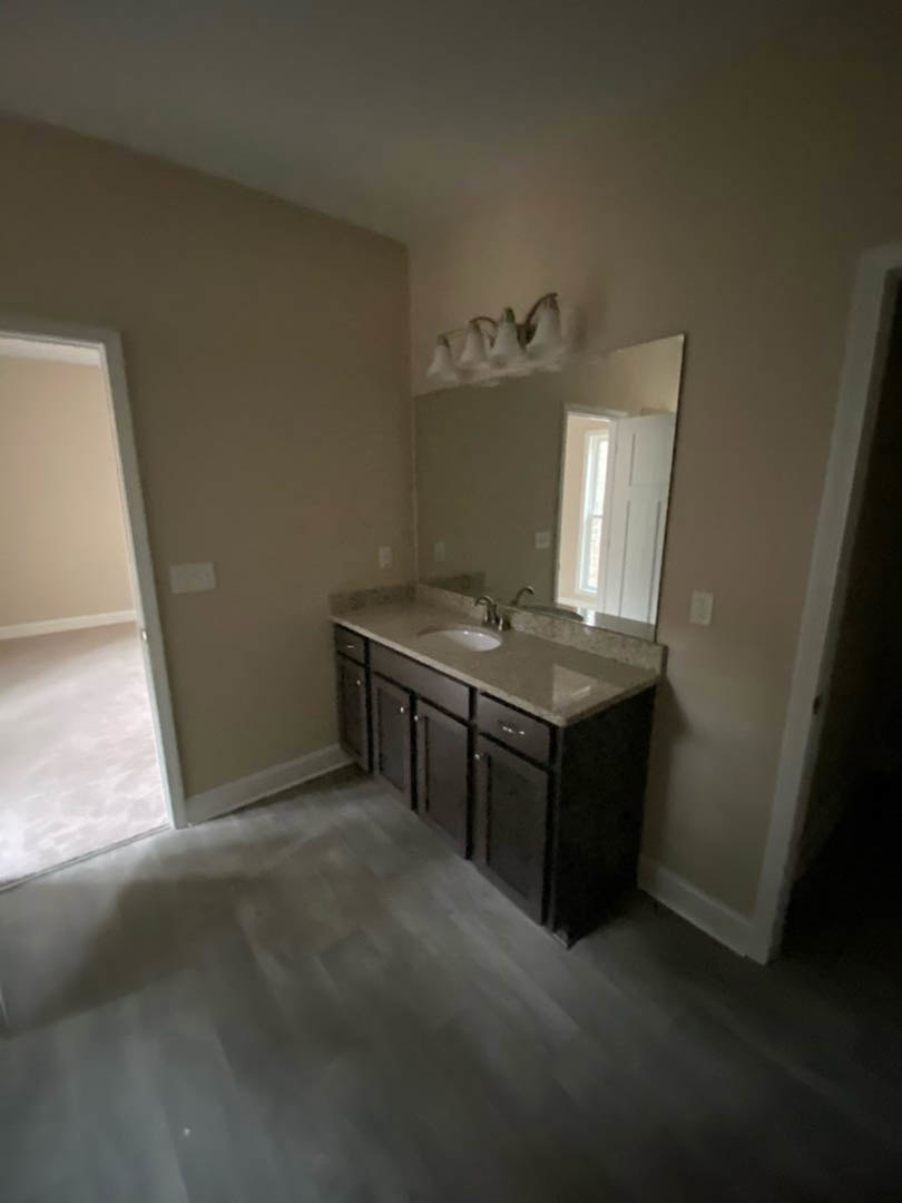 Modern bathroom with white tile walls and floor, rectangular sink with chrome faucet, large frameless mirror above vanity, minimalist cabinetry and drawers.