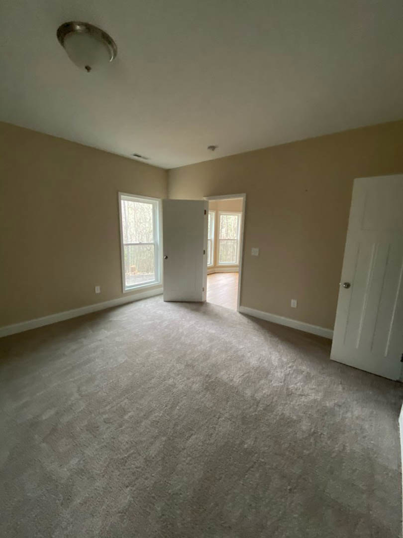 Bright room with white walls, open white door with silver handle, large window with white trim, light fixture on ceiling, light wood flooring