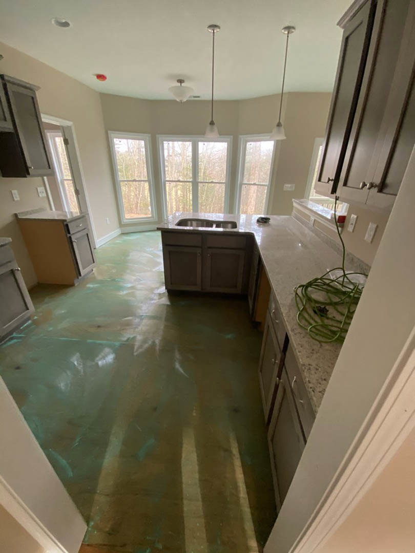 Modern kitchen featuring white tile backsplash, stainless steel sink under large windows, light wood cabinetry, stone countertops, and neutral flooring.