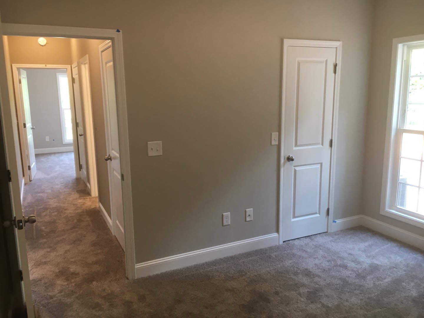 Hallway with white carpet, two white doors, white walls with black trim, window, and light switch