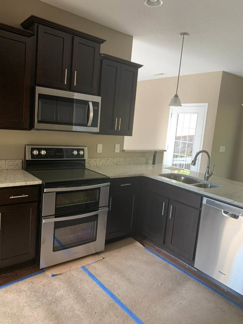 Dark wood kitchen cabinets, stainless steel stove and microwave, white door with glass window, light countertops, neutral walls