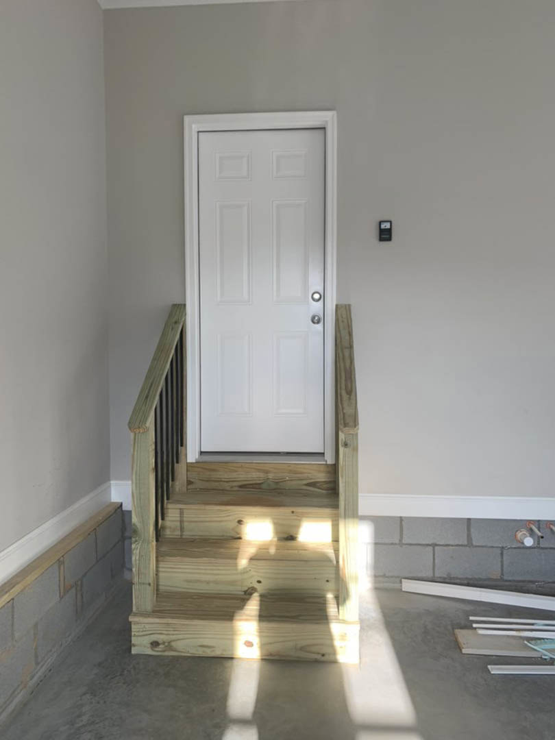 White paneled door with silver hardware beside wooden staircase featuring light oak treads and white risers, set against smooth white walls with crown molding.