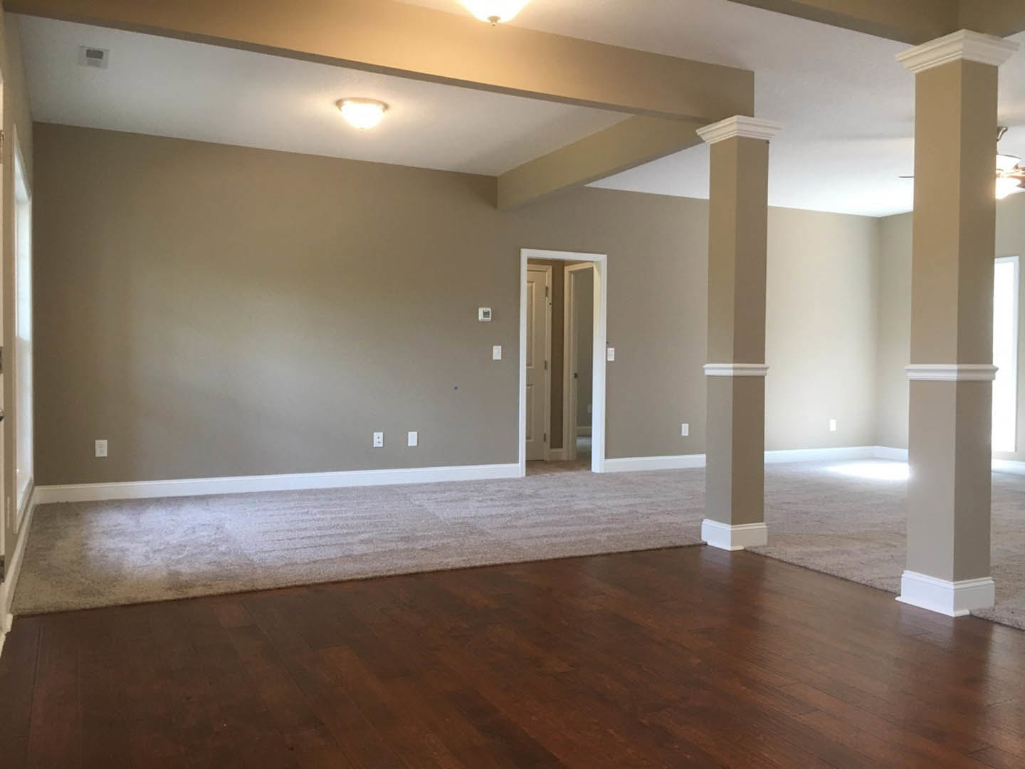 Hardwood floor with white column, open doorway, brown and white walls, ceiling light fixture
