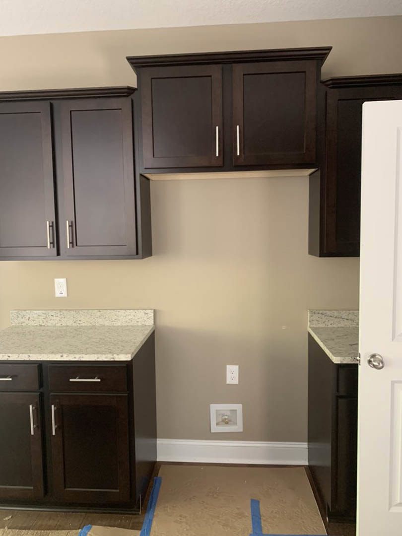 Kitchen with dark wood cabinets, marble countertops, white walls, blue tape marking on the floor, and stainless steel appliances