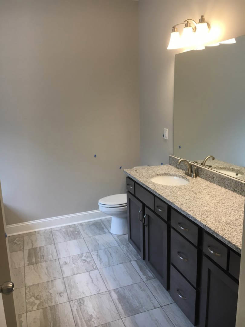 Bathroom with marble countertop, undermount sink, white toilet, tile flooring, and brushed metal light fixture