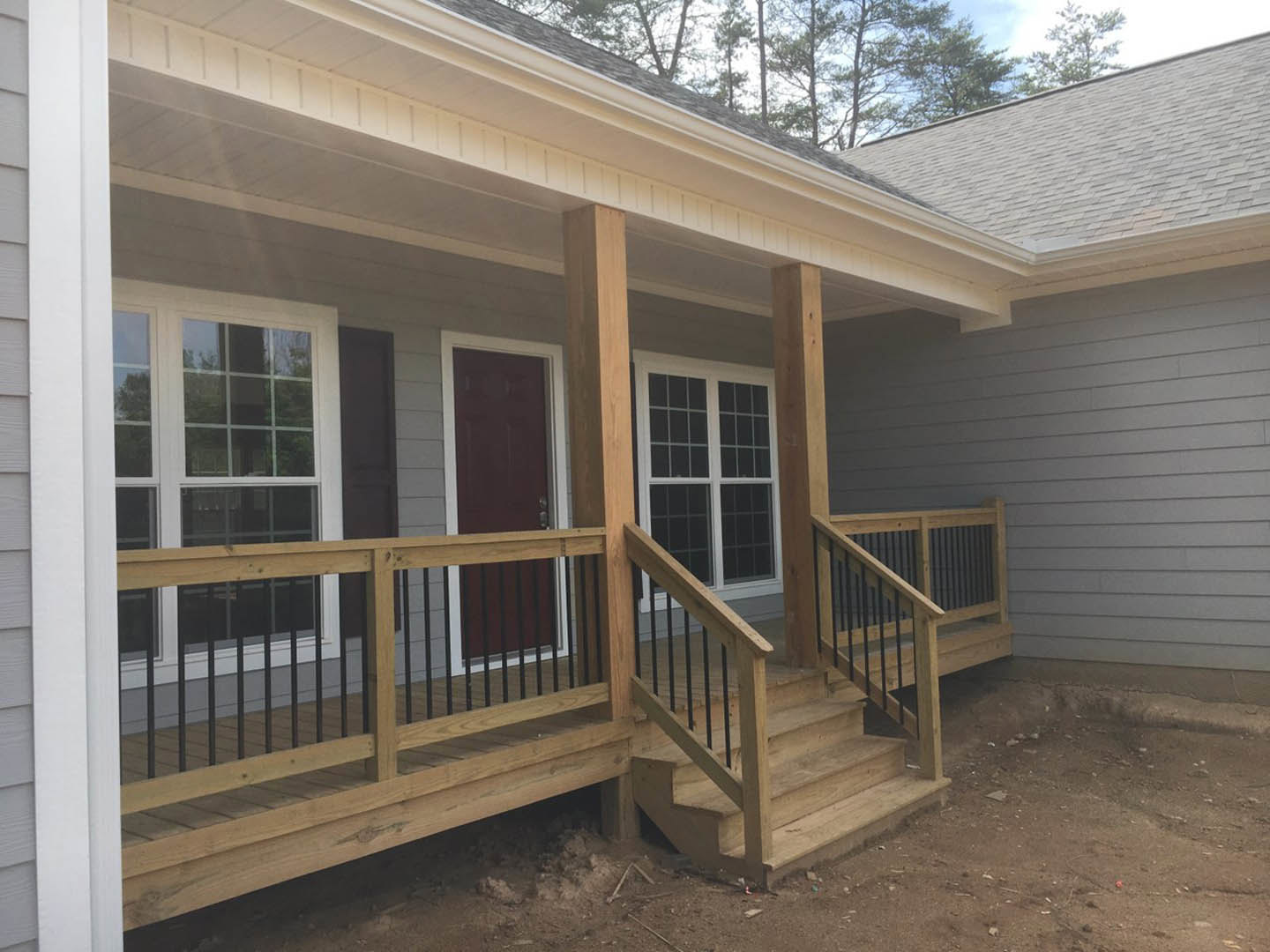Two-story home with gray siding, wooden porch and stairs, black metal railings, white-framed windows, and surrounding trees