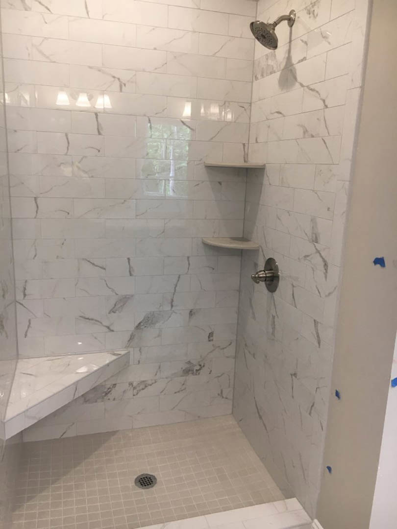 Marble tile shower walls with chrome shower head, marble countertop, and white tile reflecting light in a modern bathroom