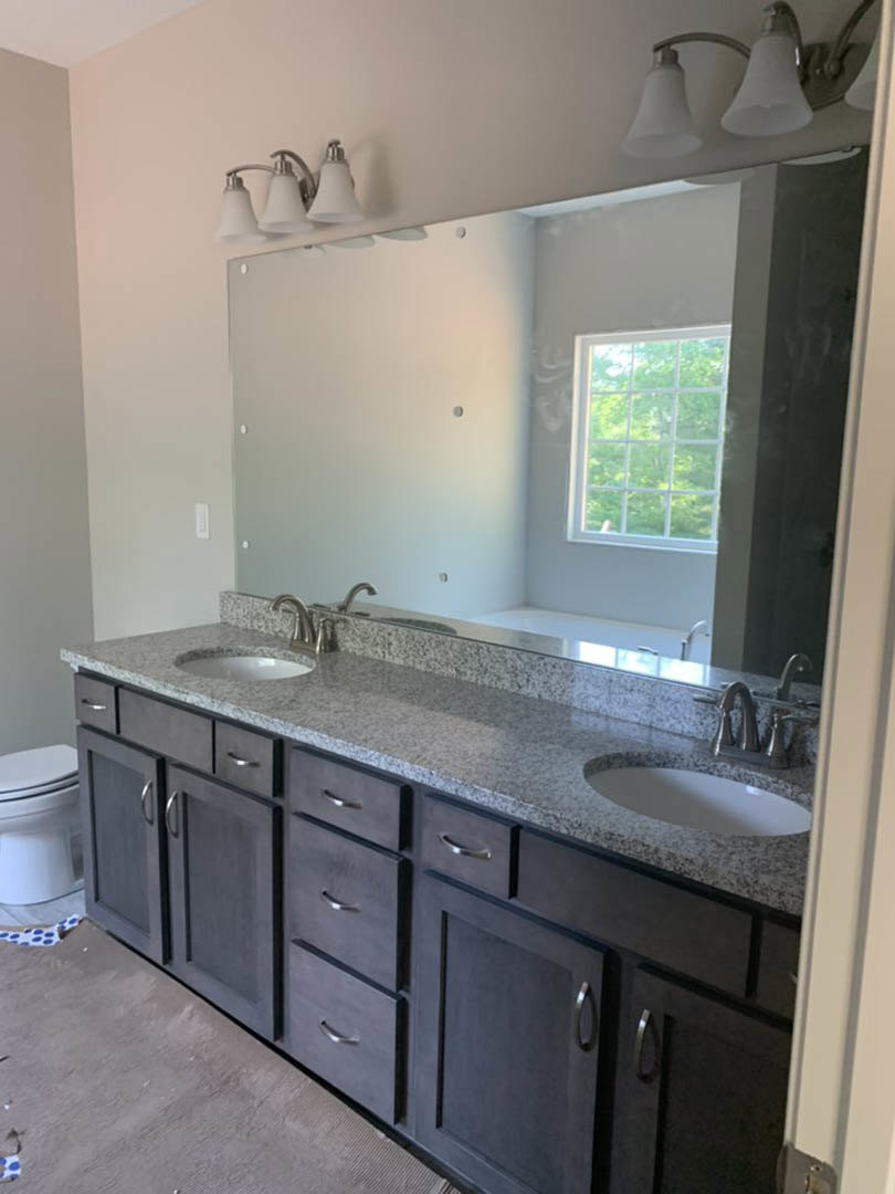 Bathroom featuring a wide framed mirror above a white sink, multi-pane window, three-light fixture, tiled walls, and cabinetry with drawers.