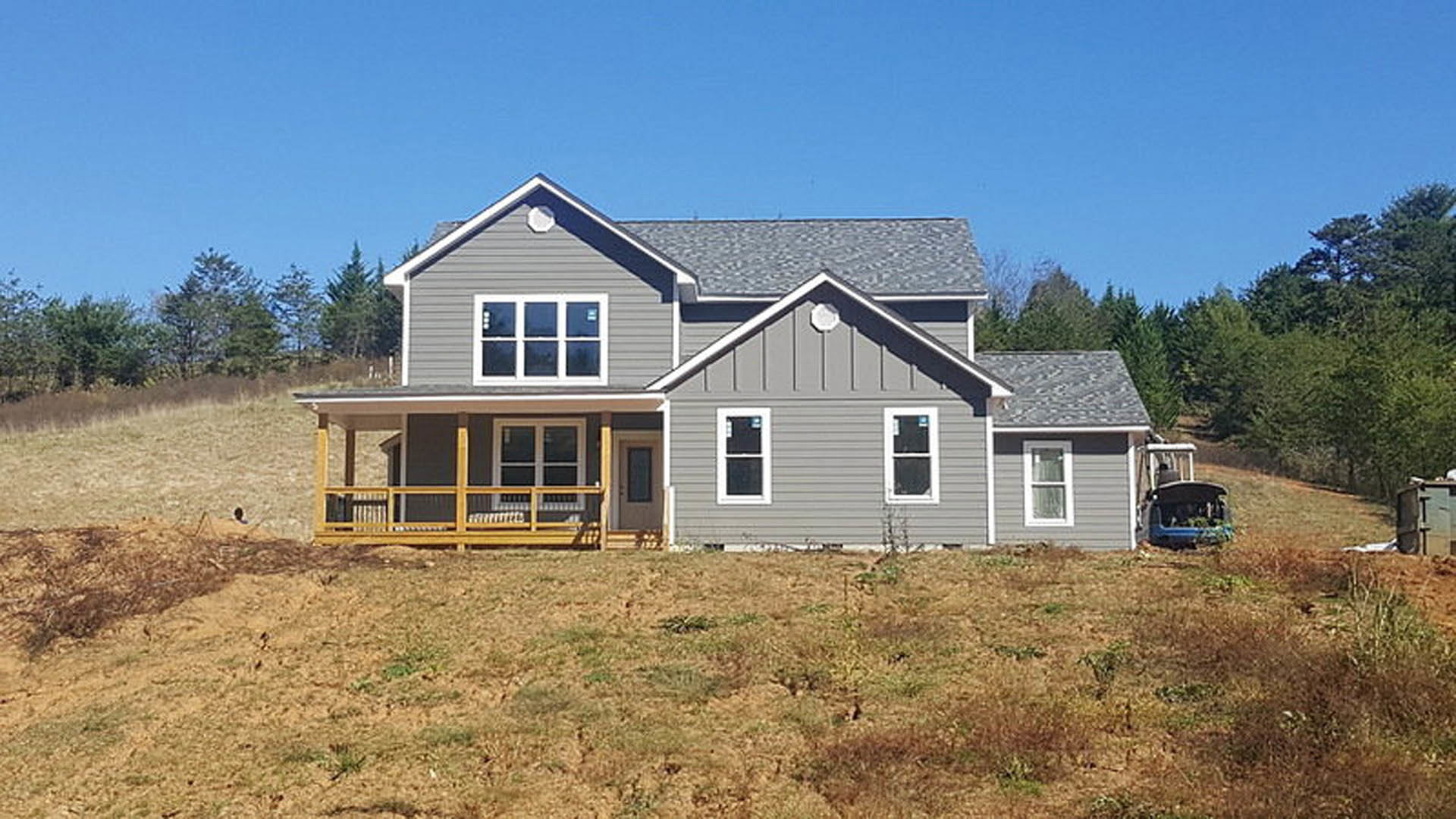 White-framed window with a small sign, wooden porch railing, light siding, and landscaped front yard with grass and trees