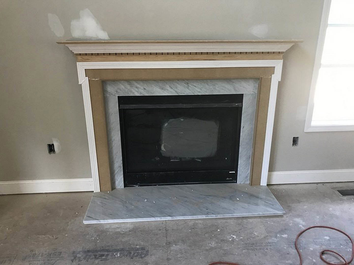 Modern wood-burning fireplace with black metal screen set into a white wall, light hardwood floor, and built-in shelf above hearth
