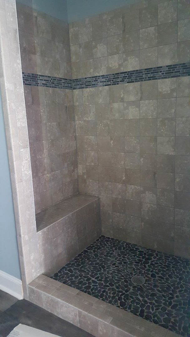 Shower featuring a stone floor, built-in stone bench, brick accent wall with black border, and tiled surfaces.