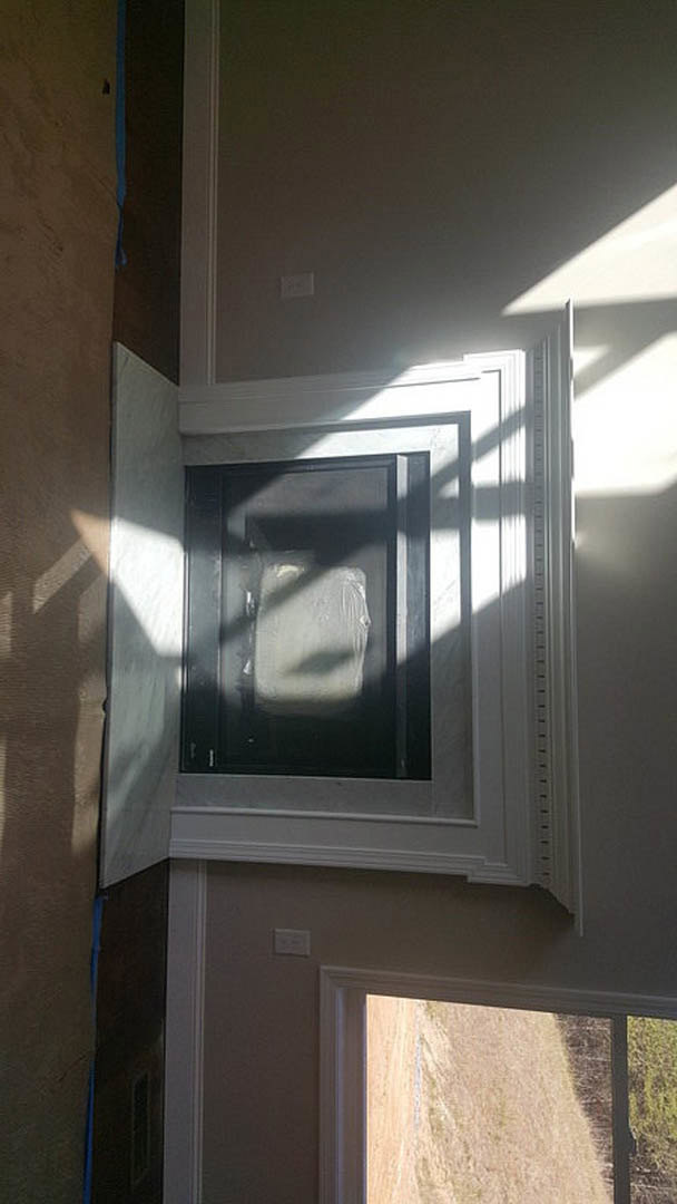 Large rectangular window set in a dark-walled room, sunlight casting shadows on the interior, view of grassy field and blue sky outside.