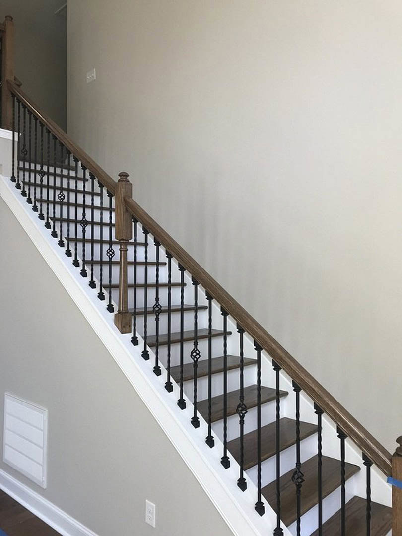 Wooden staircase with black metal railings, white walls, and a rectangular door with a black handle