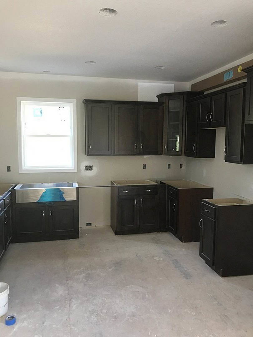 Modern kitchen featuring dark wood cabinets, light stone countertops, stainless steel appliances, and a wide window above the sink with natural light illuminating hardwood floors