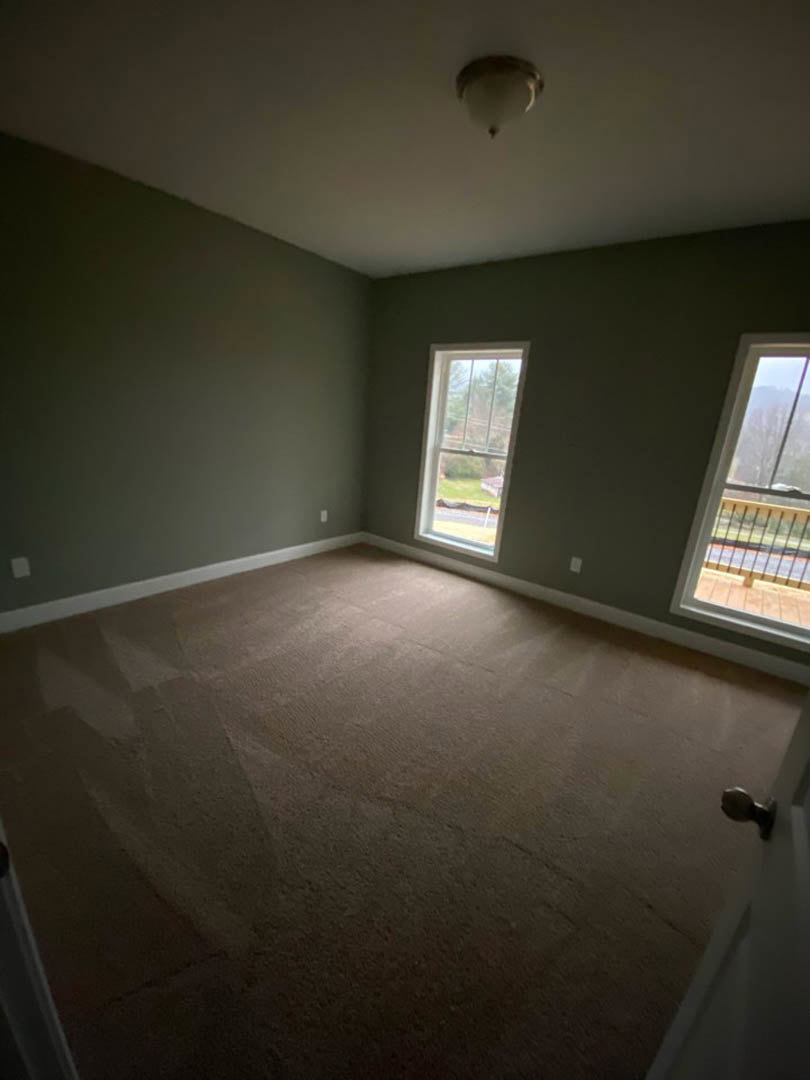 Carpeted room featuring two windows, one overlooking a lawn and the other with a railing, white plaster walls, ceiling-mounted light fixture, and a close-up of a door knob