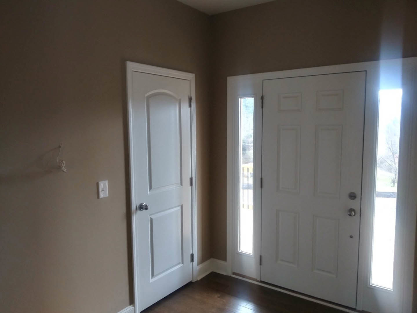 Dark wood flooring with white trim, two white paneled doors with silver doorknobs, white walls, and a light switch with a bell in a residential interior room