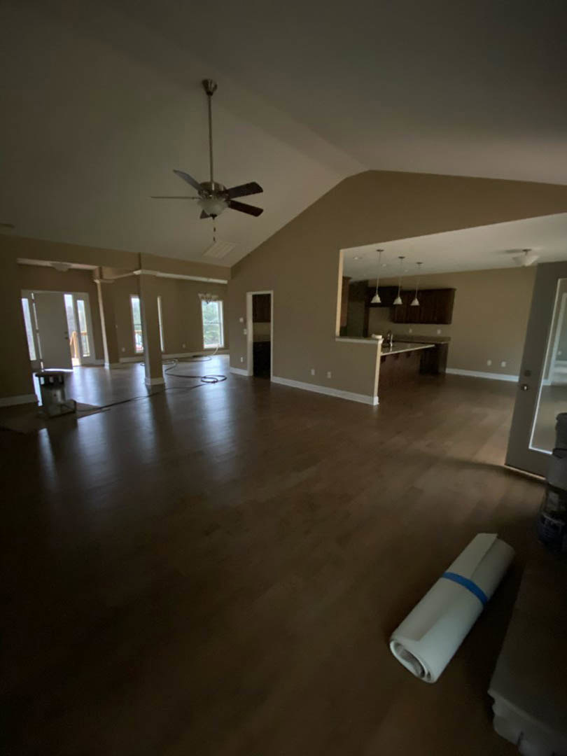 Ceiling fan with light fixture mounted above wood flooring, white plaster walls, and partially unrolled carpet in a residential interior.