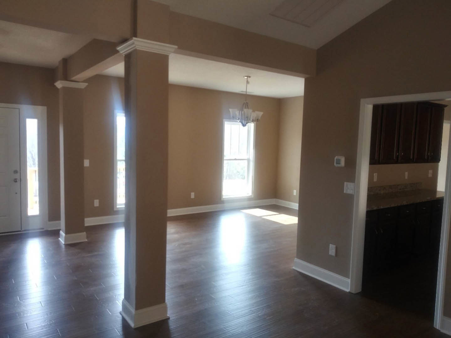 Open room with wood flooring, white plaster walls, wood cabinetry, white-framed window, and ceiling-mounted chandelier