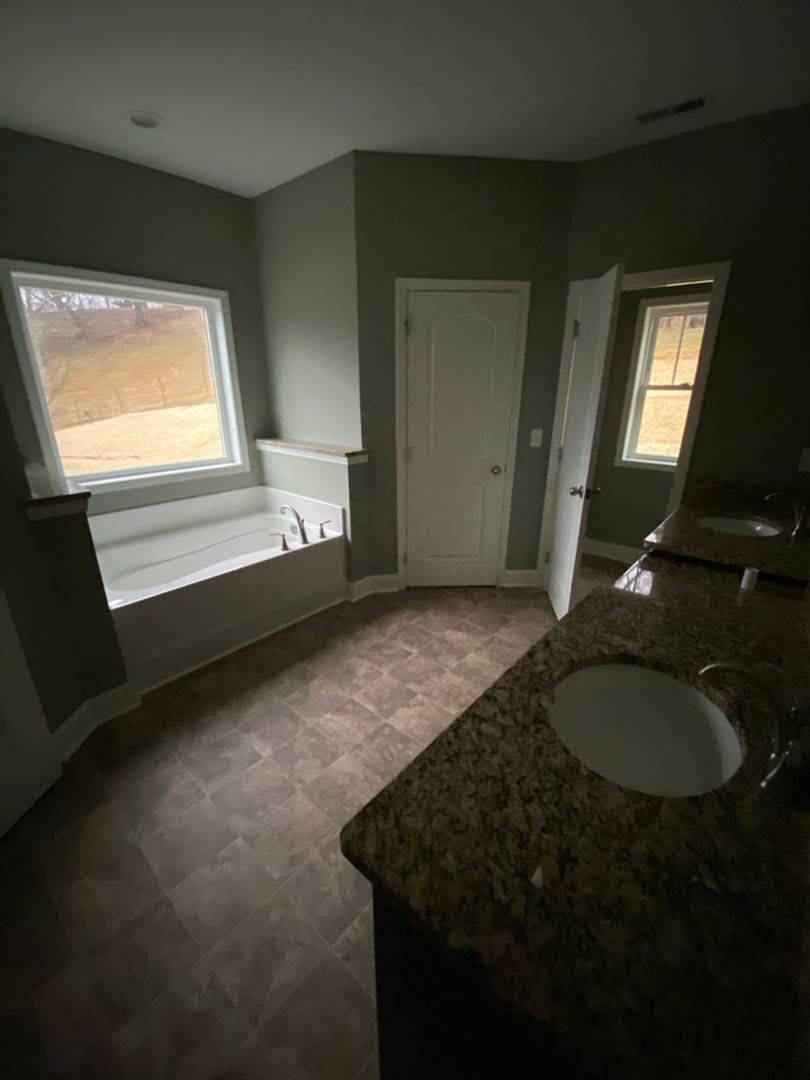 Bathroom with marble countertop vanity, undermount sink, freestanding tub, white toilet with metal handle, white door with silver knob, tile flooring, large mirror, window