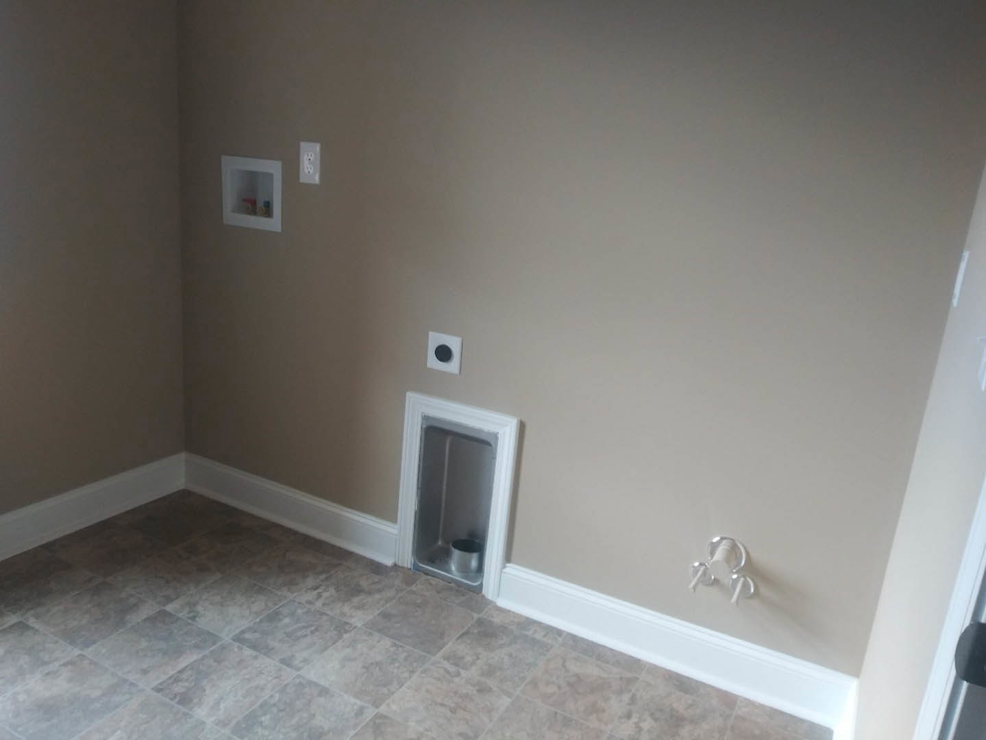White plaster wall with a small circular metal insert, adjacent to built-in shelving and light wood flooring