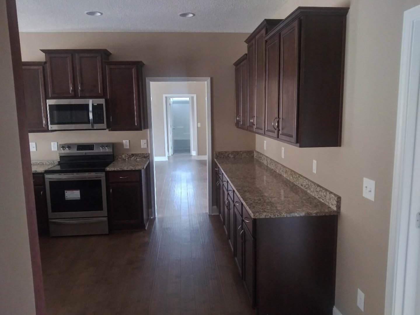 Kitchen with dark wood cabinets, granite countertops, open microwave, stainless steel stove, white door with illuminated hallway beyond