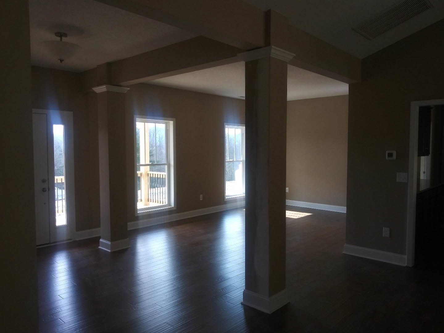 Room with light wood flooring, white plaster walls, large window with white frame and metal railing, and white door with silver handle