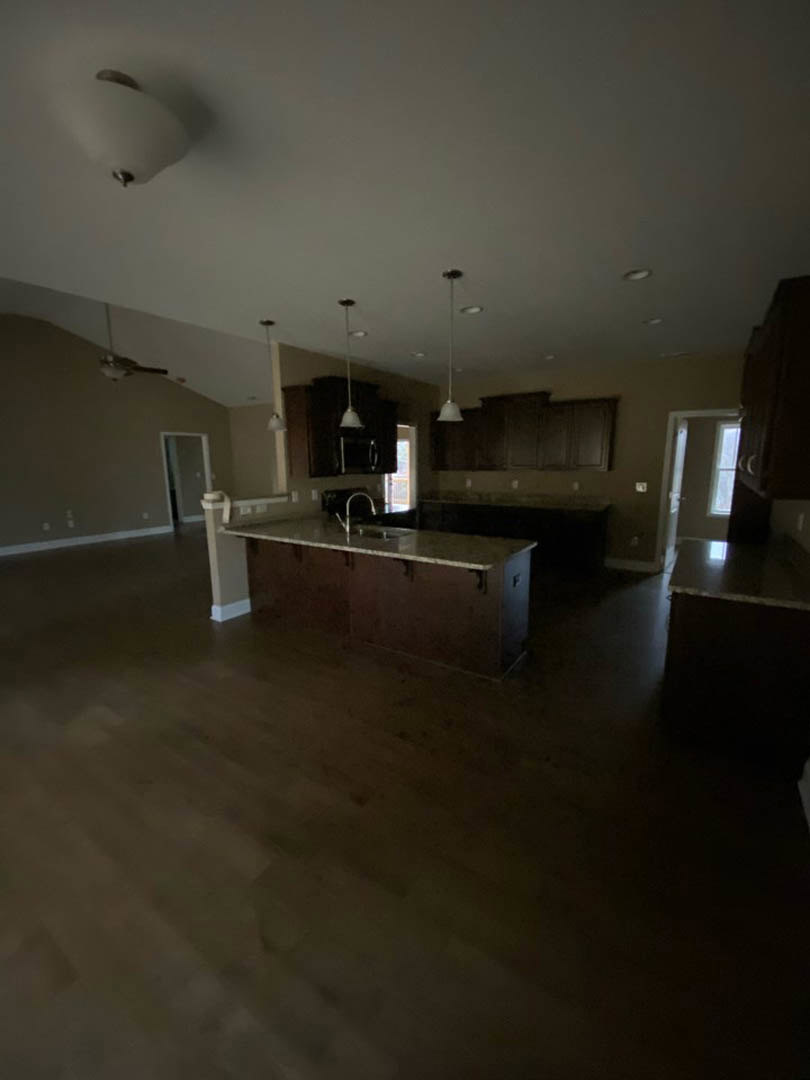 Spacious kitchen featuring a large central island with stone countertop and built-in sink, pendant lighting overhead, laminate flooring, and white plaster walls.