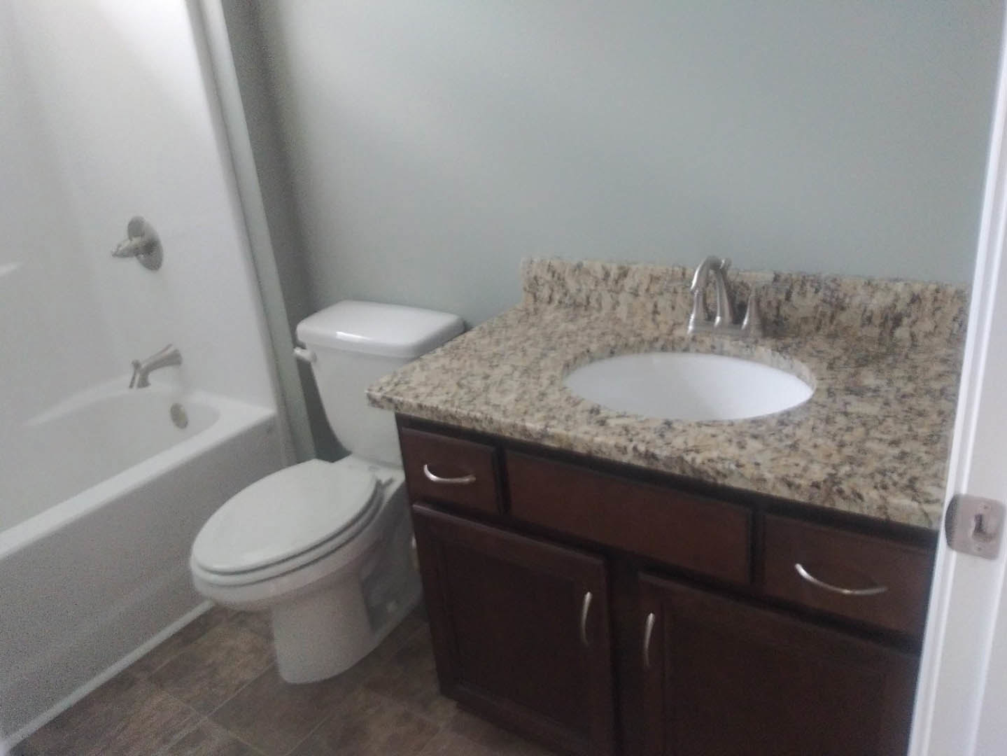Marble countertop vanity with undermount sink, chrome faucet, and adjacent white toilet in a tiled bathroom with partial wall and mirror visible