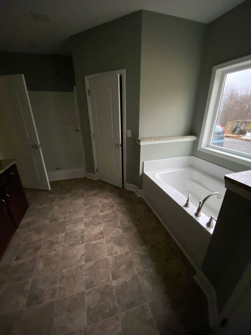 Bathroom with freestanding bathtub, white tile floor, modern sink with silver faucet, white door, window overlooking trees and parked car