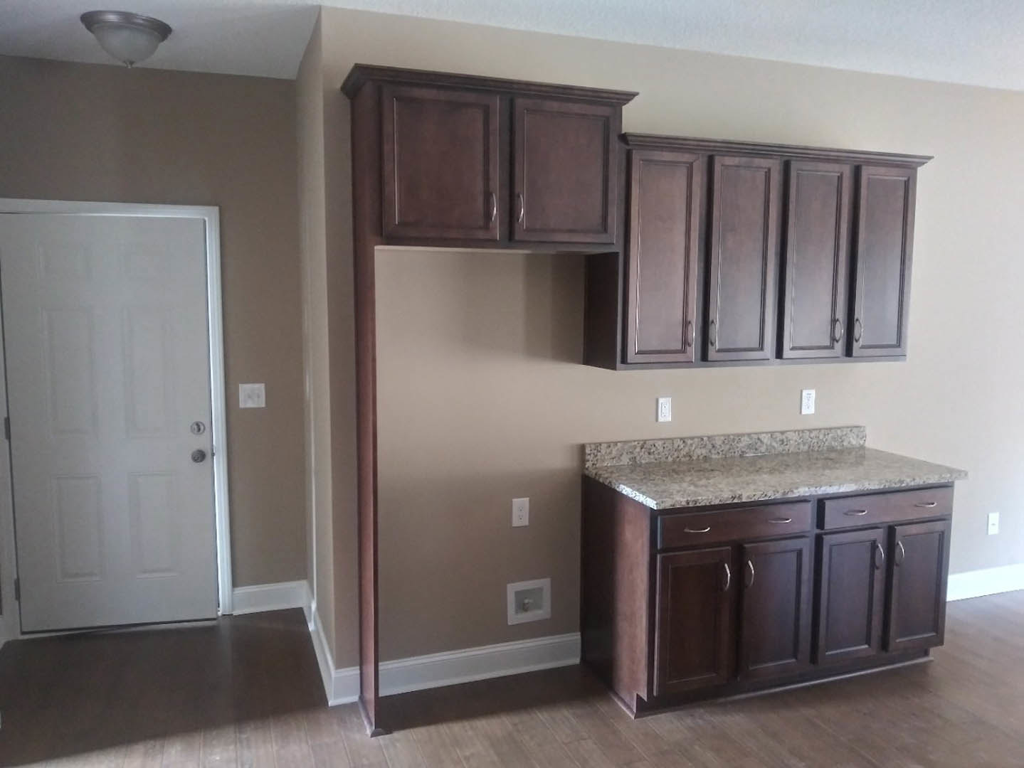 Dark wood kitchen cabinets, granite countertops, stainless steel sink, white door with silver handle, wall-mounted light fixture, marble kitchen island, close-up of cabinet drawer