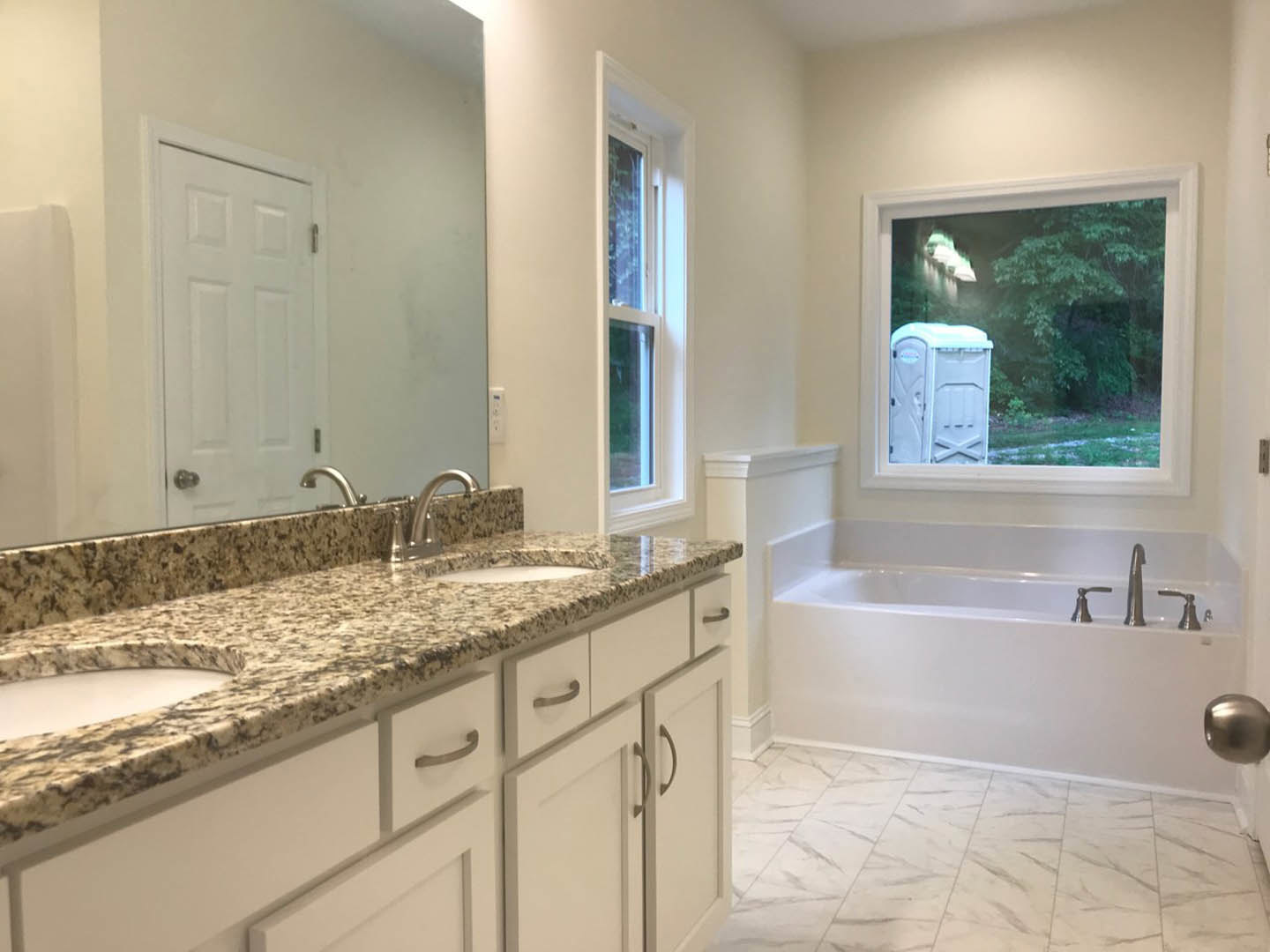 Bathroom with marble countertops, freestanding bathtub, white framed window, silver faucet, tile flooring, and white cabinetry