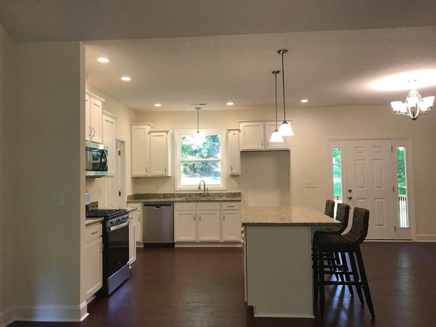 Modern kitchen with white cabinetry, black and silver oven, built-in dishwasher, bar-height counter with stools, and window framed in white