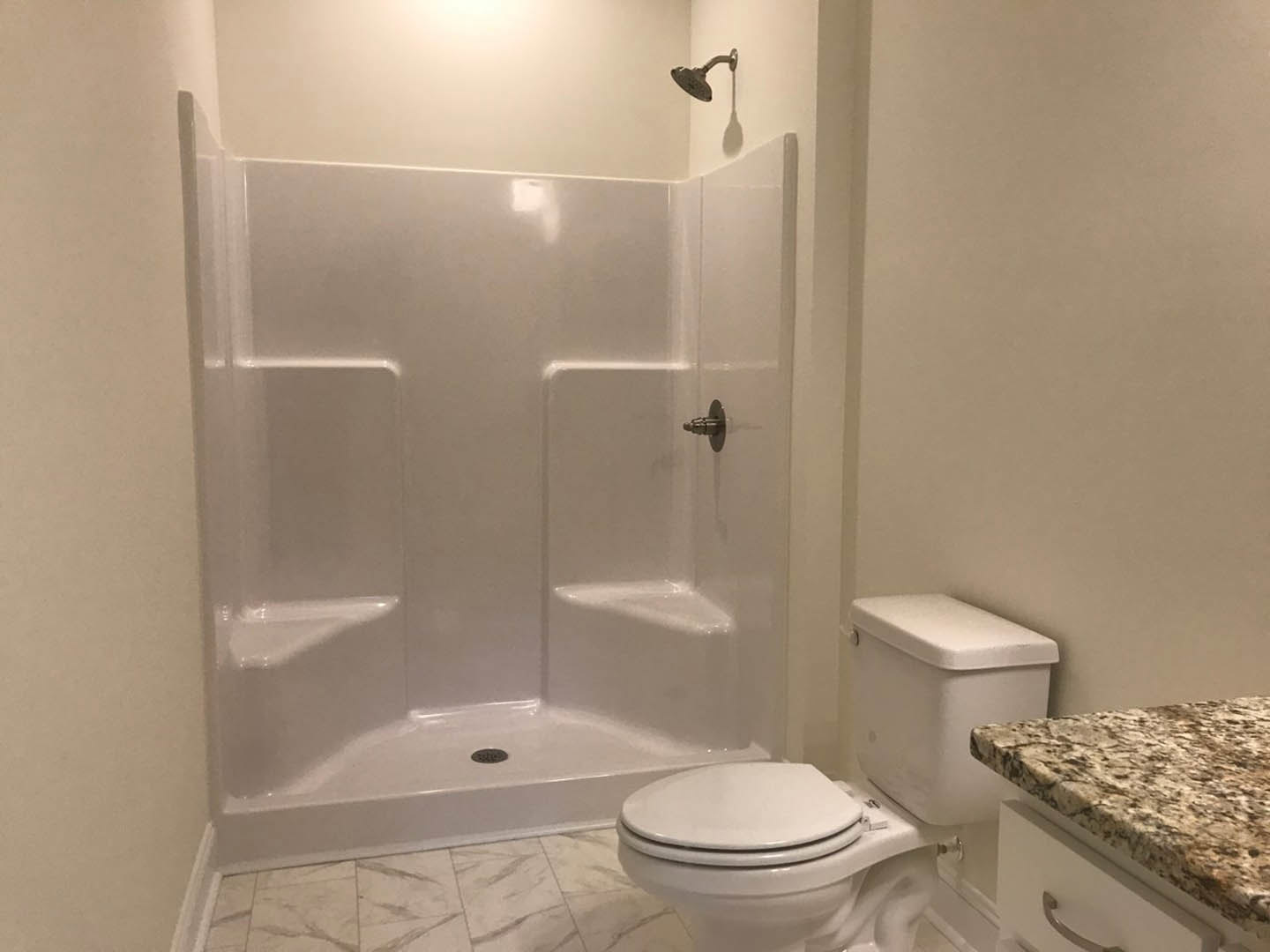 Modern bathroom featuring a white toilet with open lid, white vanity with drawers, silver faucet, and glass-enclosed shower with silver handle, set against light tile walls.