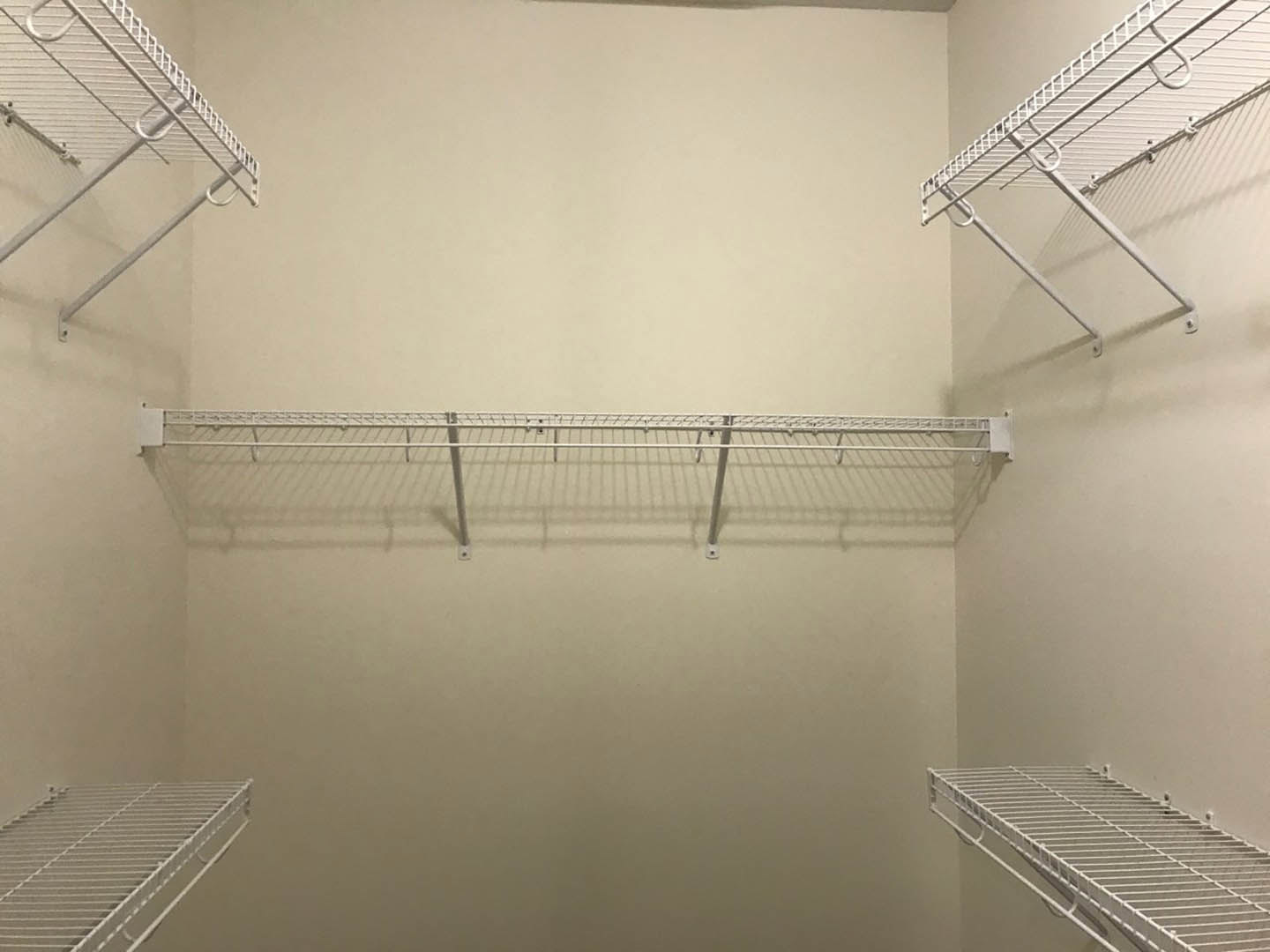 White metal shelf with hooks mounted on a plaster wall in a bathroom, surrounded by white finishes and minimal decor.