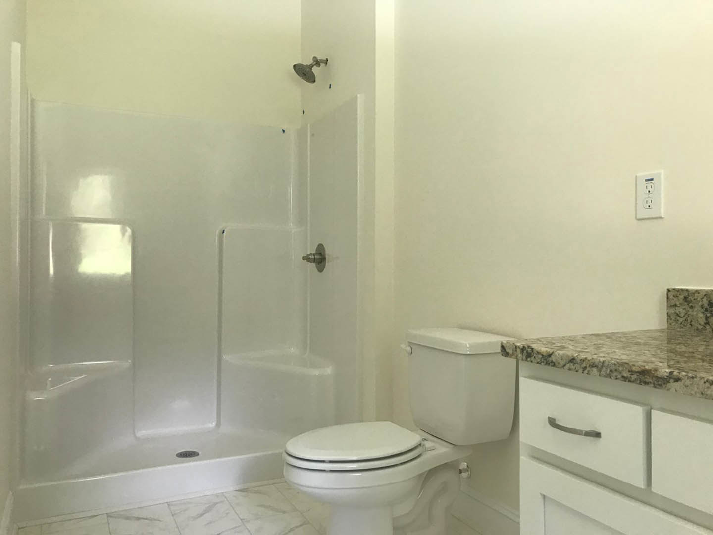 White tile bathroom with glass shower enclosure, chrome shower head, modern toilet, and wall-mounted faucet