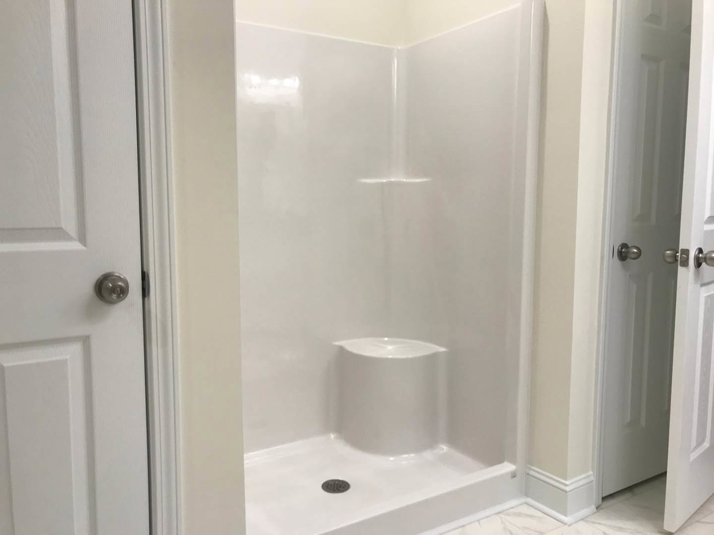 White tile shower stall with glass door, silver handle, and built-in step, adjacent to a white bathtub with visible drain.