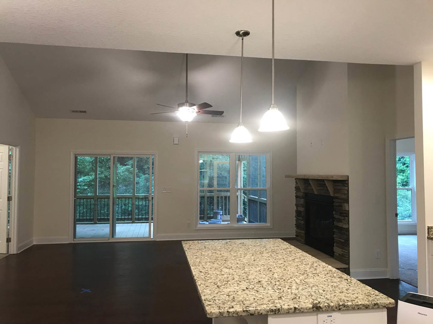 Open kitchen with stone fireplace, ceiling fan, light cabinetry, sliding glass door to deck, and window overlooking outdoor view