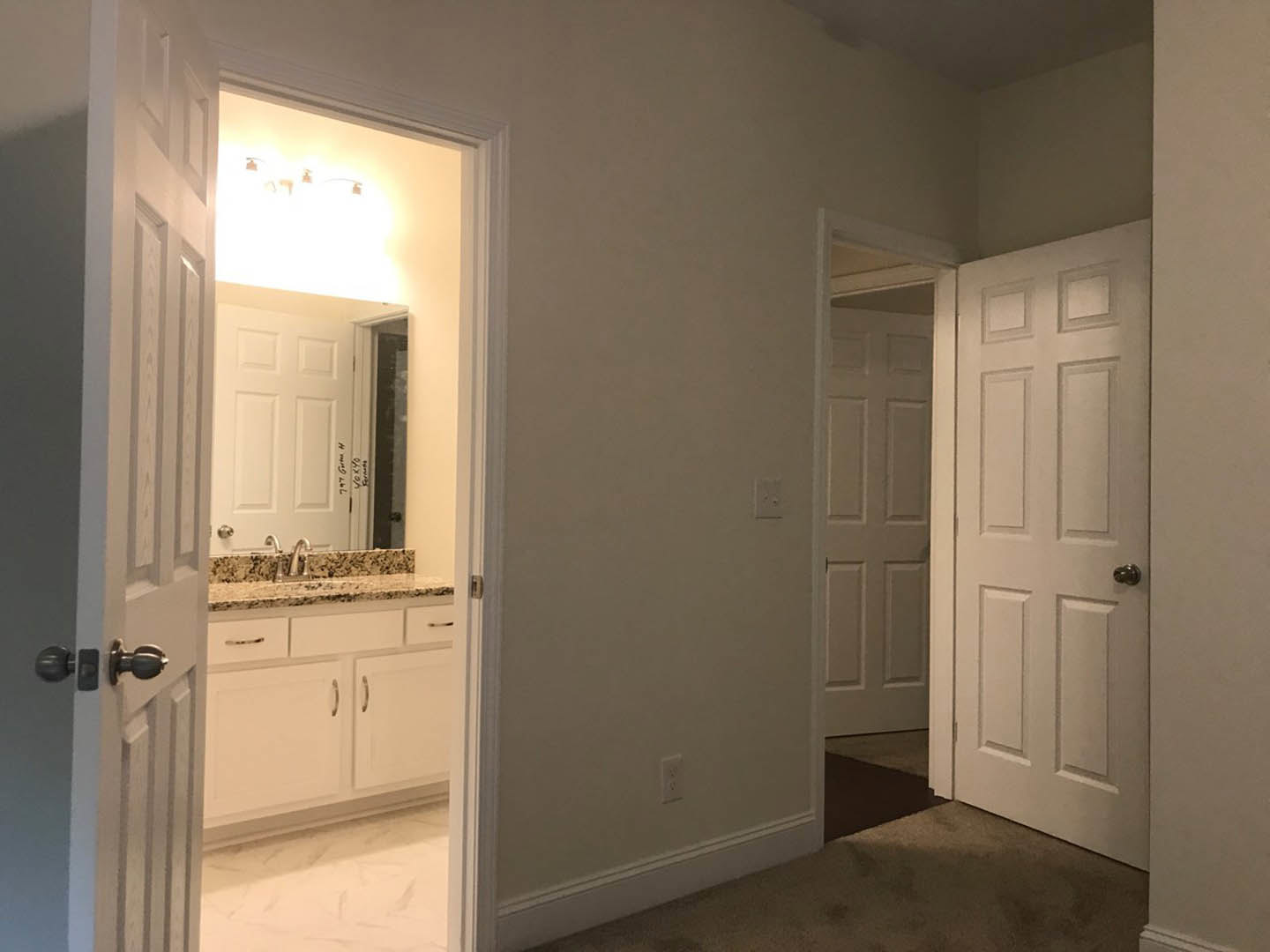 Bathroom with white paneled doors, silver door handle, marble countertop, light tile flooring, and white cabinetry.