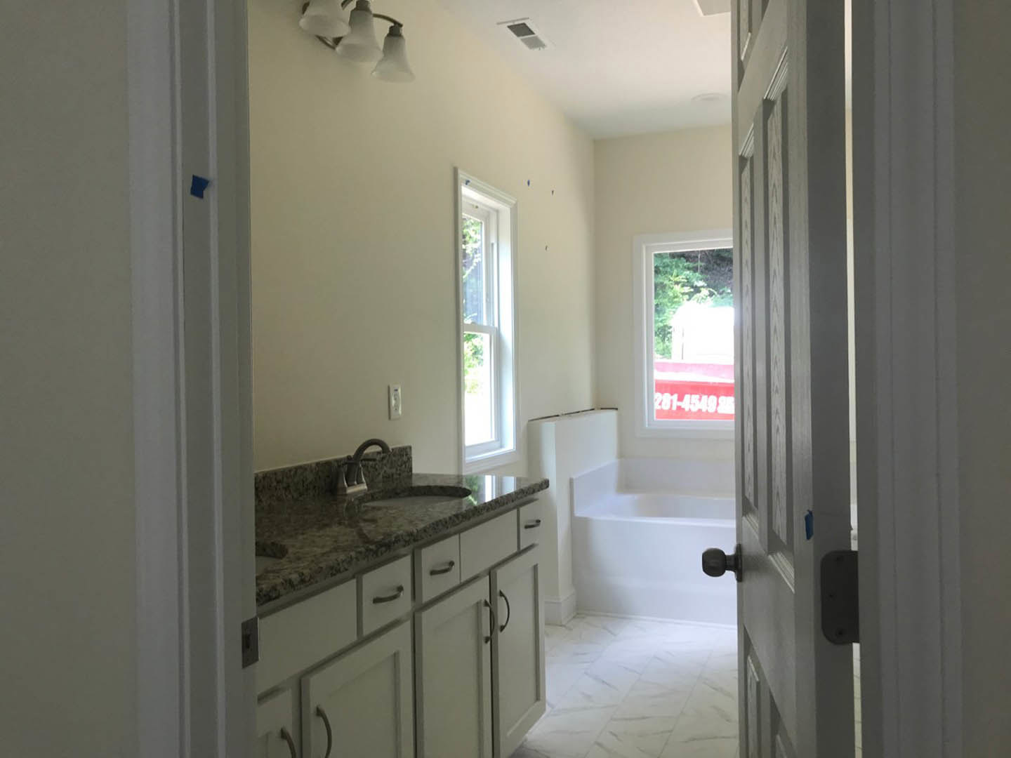 Modern bathroom featuring a freestanding white bathtub, rectangular sink with chrome faucet, light gray tile walls, white framed window, and sleek black light fixture.
