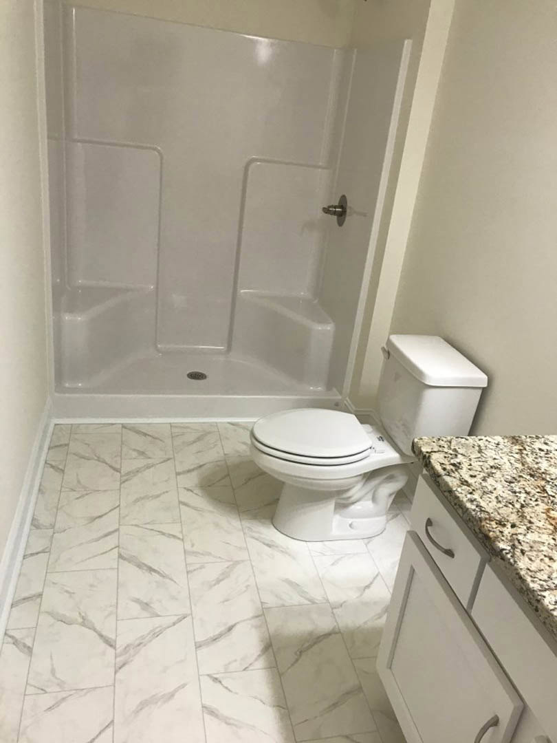 Modern bathroom with white tile walls, glass shower enclosure, open shower door, white toilet with lid up, and white vanity cabinet with metal handle