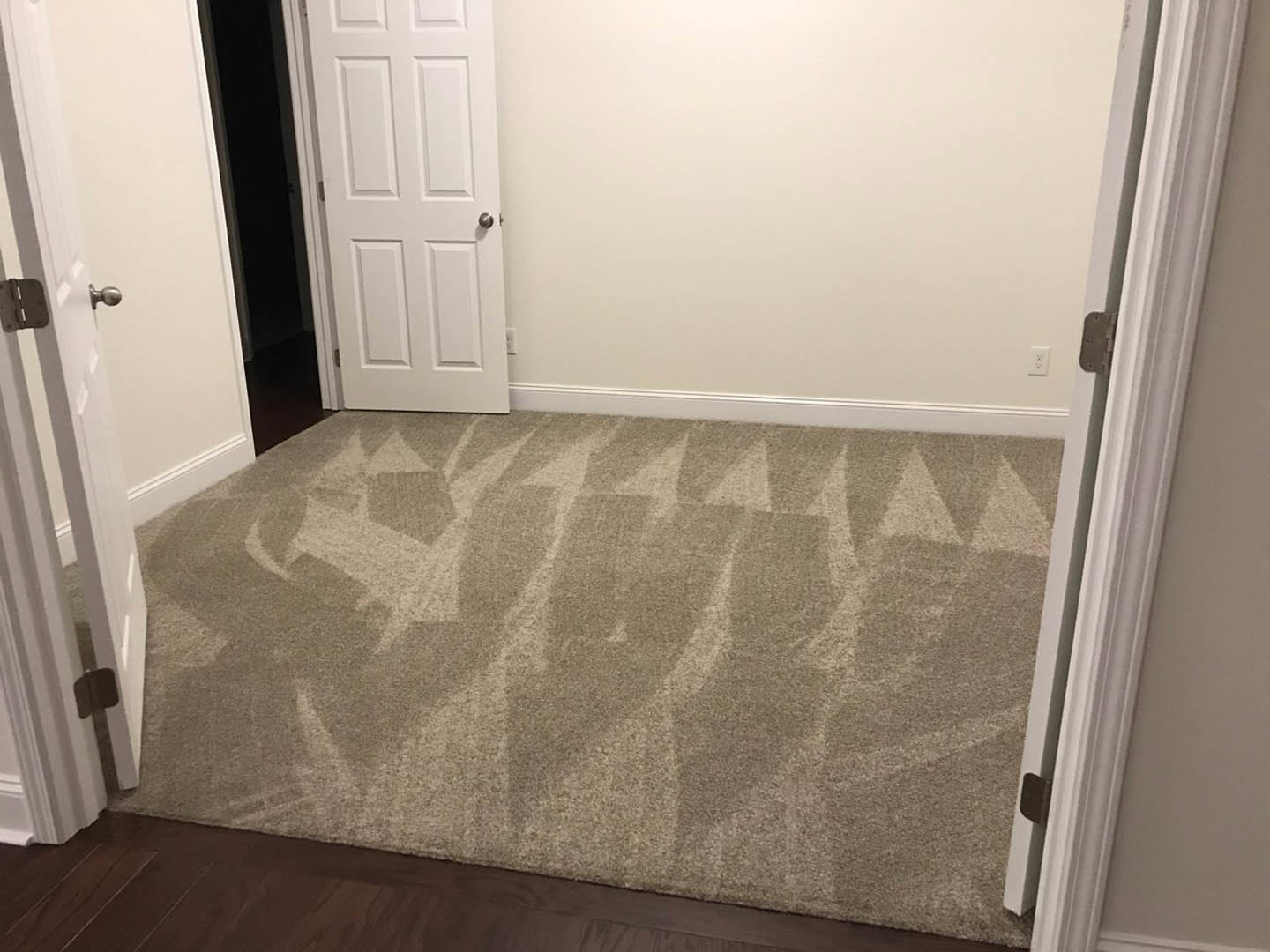 Beige carpet covering floor, white door with silver handle and hinge, white walls and ceiling, black door with white frame