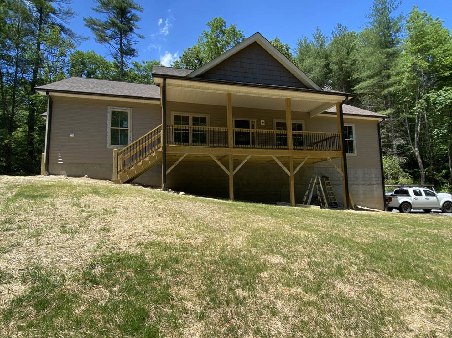 Two-story wooden house with covered porch, white trim, front stairs, manicured lawn, and a white truck parked in driveway; large windows and balcony visible.
