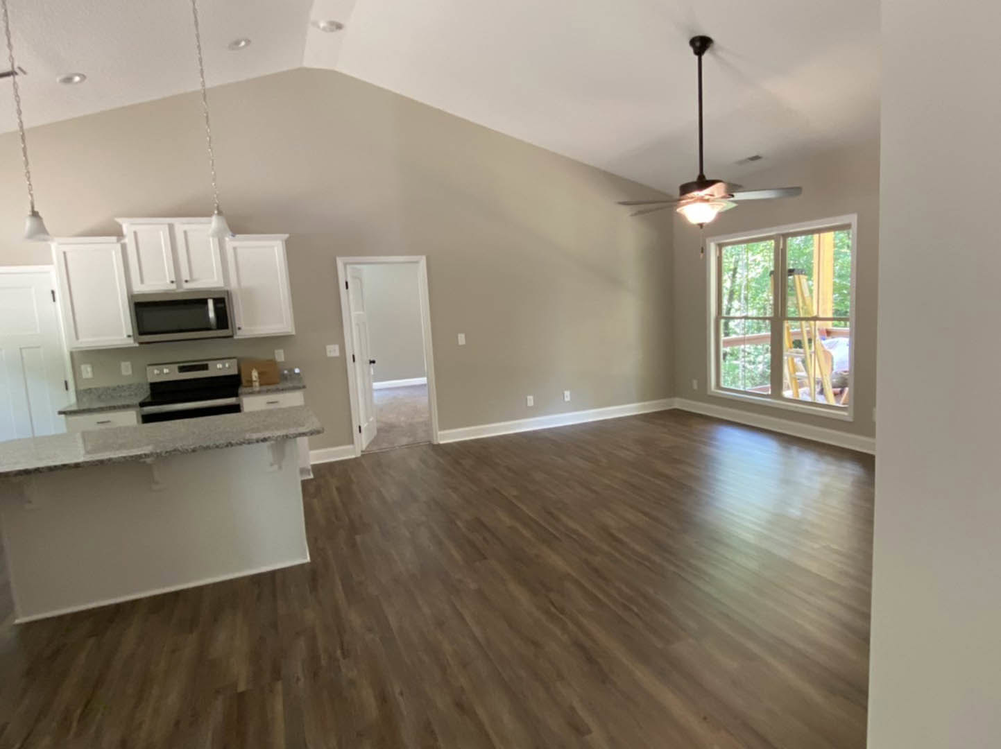 Open-concept kitchen and living room featuring hardwood floors, white cabinetry, black hardware, stone countertop, large window, and white door with black handle