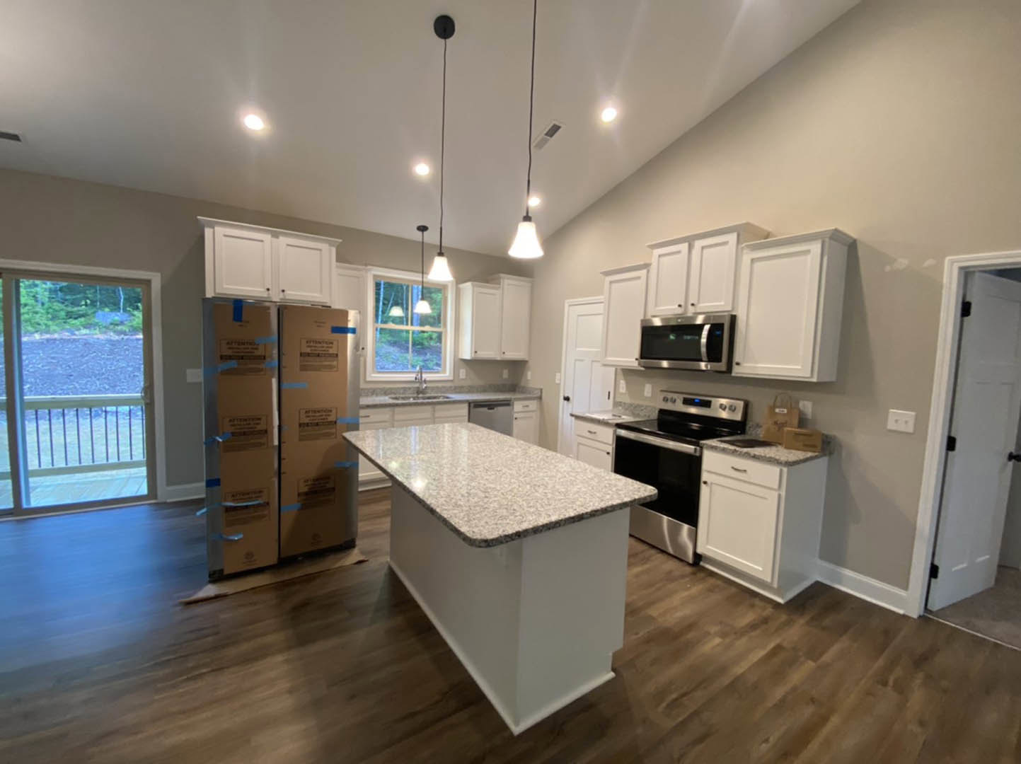 Spacious kitchen featuring a white marble-topped island, large window with natural light, sleek cabinetry, stainless steel appliances, and light wood flooring