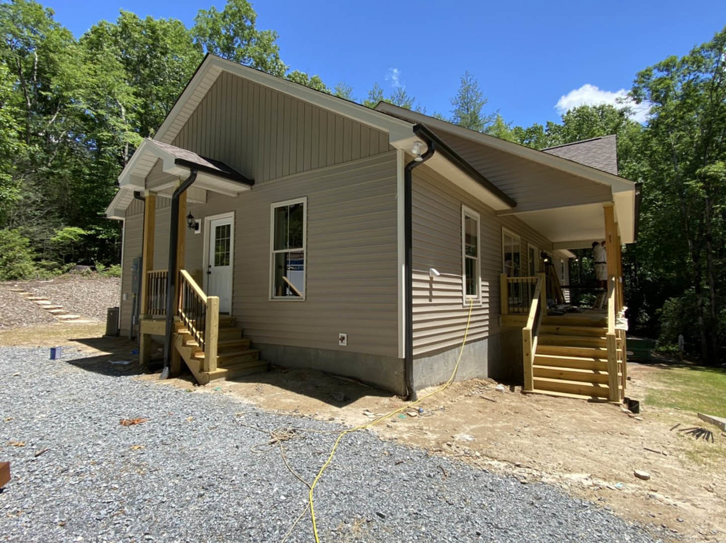 Two-story home with gravel driveway, wooden stairs with metal railing leading to covered porch, white framed windows, white door with window, yellow garden hose on ground